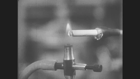 1950s: UNITED STATES: cigarette in clamp during experiment. Bubbler in lab. Stock Footage