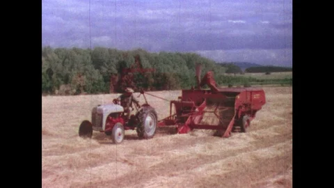 1950s: UNITED STATES: Tractor pulls combine harvester in field. Farmer ploughs f Stock Footage 88876915