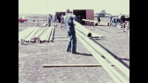 1950s: UNITED STATES: workers lay out metal pipes on ground. Man lifts pipe from Stock Footage 98009896