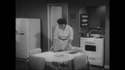 1950s: Wife sets table in kitchen, husband enters, eats from pot, woman turns, Stock Footage