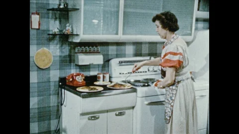 1950s: Woman prepares plates of food at stove. Woman serves plates to family at Stock Footage