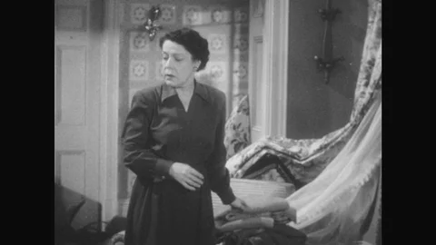 1950s: woman puts down blankets in destroyed living room as man in jumpsuit Stock Footage
