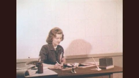 1950s: Woman sits at desk turning pages of book. Woman enters room with large Stock Footage