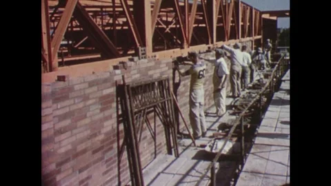 1950s: Workers build wall from bricks. Acme building. Man picks up bread bun and Vídeos de archivo 75170723