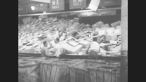 1950s: Workers toss parcels into tubs. Workers sort mail in a large room. Stockbeeldmateriaal 79978874