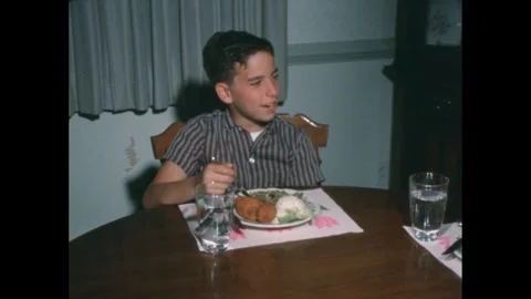 1950s: A young boy sits at a table, focused on his plate as he enjoys a hearty Stock Footage 280855408