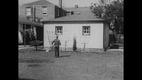 1950s: Young boy stacks bricks in back yard near garage. Boy runs from back yard Stockbeeldmateriaal 295213330