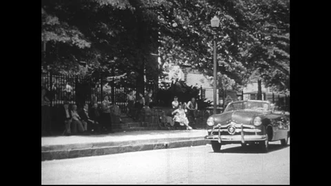 1950s:Convertible drives down suburban street. Car is parked in front of gas Stock Footage