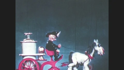 1950s:Horse drawn fire engine puppet trots by. Old man puppet jumps, runs. Stock Footage 79474989