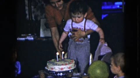1951: mother helping a two year old boy blowing out candles at birthday party Stock Footage