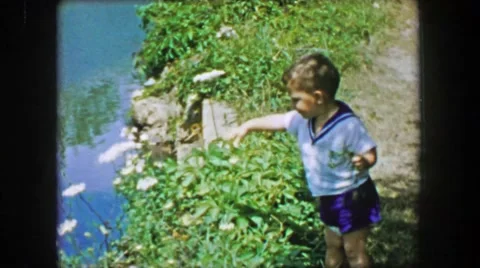 1955: Toddler boy throwing stick attempt into calm reflecting pond waters. Stock-Footage 64569923