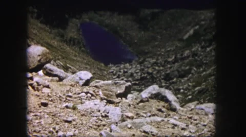 1958: a blue lake like a gem in the heart of a hill with rocks scattered Stock Footage