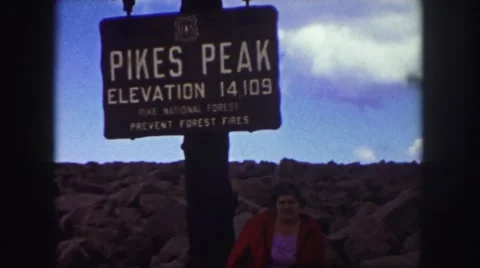 1958: lady wearing red coat under pike's peak sign rocks partly cloudy skies Stock Footage
