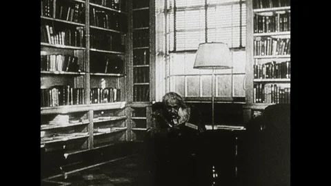 1960s: Albert Einstein in library, walks to shelf. Einstein puts book on shelf, Stock Footage 129972089