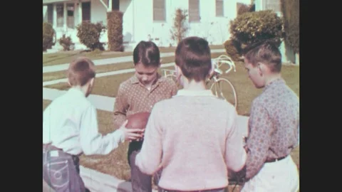 1960s: Boy gives ball to other boy, runs and grabs his bike. Two other boys Stock Footage