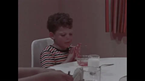 1960s: Boy at kitchen table wipes food off face. Clock on wall. Bottle of bleach Stock Footage 212809011