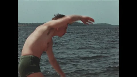 1960s: Boy standing on pier, practicing swimming stroke. Boys on pier practicing Stock Footage 256051633