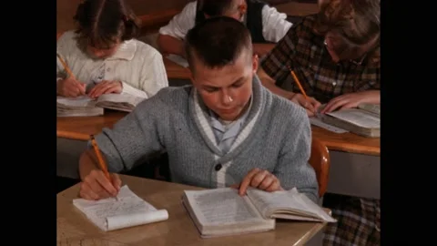 1960s: boy struggles with work in class. Boy reads from book. Boy writes notes Stock Footage 219965675
