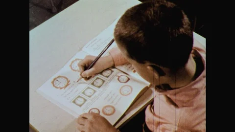 1960s: boy uses pencil to do math problem with clocks pictured, pencil tip Vídeos de archivo 126010600