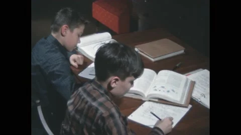 1960s: Boys writing at table, boy opens book, zoom in on book. Farm equipment in Stock Footage 188534796