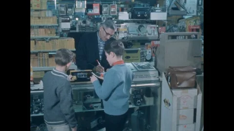 1960s: Camera store.  Boys speak to man at counter.  Man rings up sale.  Boys Vidéo 249612989