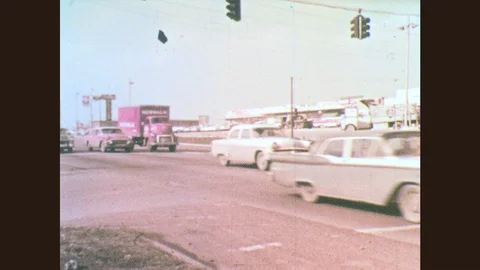 1960s: Cars pass through intersection.  Truck drives down street.  Parking lot Stock Footage 77981496