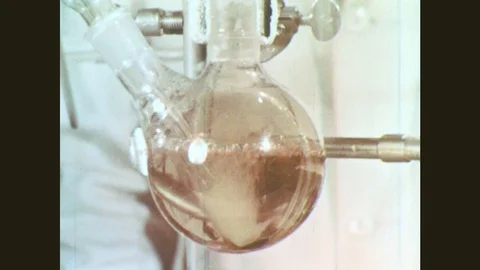 1960s: Chemical solution bubbles in glassware. Hand turns know on Sulphur Stock Footage