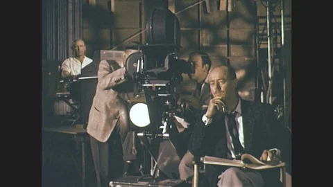 1960s:  cinematographer looks into movie camera as man with script sits nearby. Stock Footage