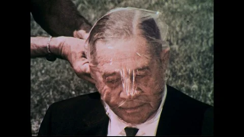 1960s: Close up, hands tie plastic bag over man's head, remove bag. Stock Footage 74588937