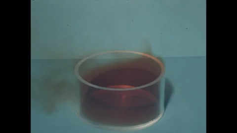 1960s: cloud of red gas or smoke swirls out of circular glass container as hand Video stock 240679201