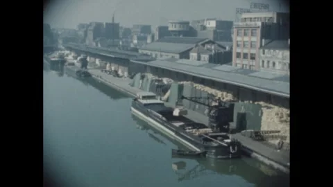 1960s: Crane unloads barge on river near industrial section of city in France. Stock Footage 283926772