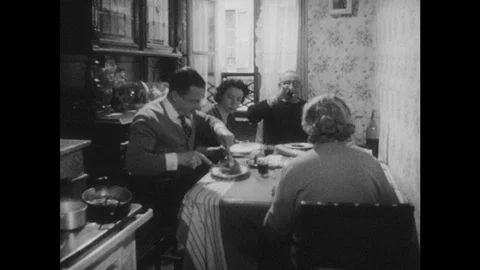 1960s: Family eats in kitchen.  Young people sit at bar.  Man slices cheese.  Stock Footage 127661615
