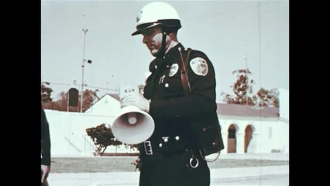 1960s: A field commander radios to another police officer as he is assisted by Vídeos de archivo 74489419