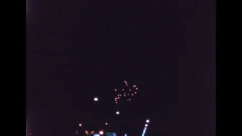 1960s: Fireworks explode in night sky over street lights. Stock Footage 112013762
