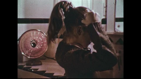 1960s: Girl applies hair spray to ponytail in front of space heater. Girl safely Stock Footage