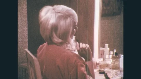 1960s: Girl in robe primps, arranges hair in vanity mirror. Boy in dune buggy in Stock Footage