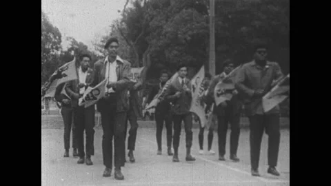 1960s: Group of Black Panthers march together across basketball court, carrying, Video stock 153549406
