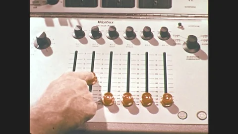 1960s: hand slides knobs on audio mixing board. men talk near machine and  giant 스톡 동영상 76596446