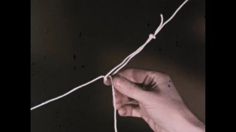 1960s: Hand traces path from sting on glass tube to loop. Hands attach silk loop Stock Footage 280054712