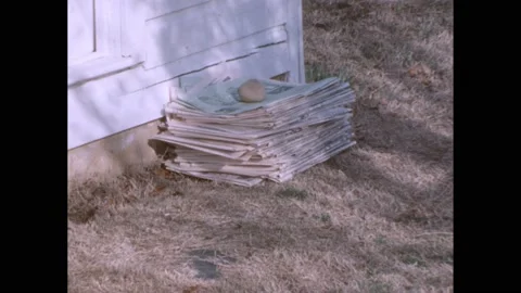 1960s: Hands holding paper. Stack of newspapers next to house, zoom out, girl Video stock 238791561