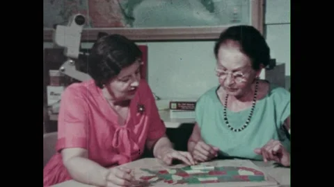 1960s: Hands move Boggle dice on table. Women talk and look at map of United Video stock 237700254