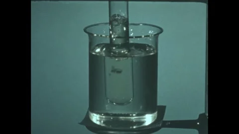 1960s: Liquid bubbles in test tube suspended in glass beaker on laboratory Stock Footage 246750067