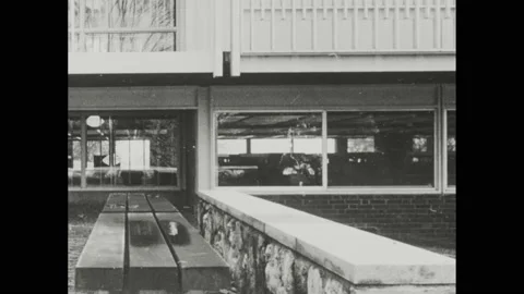 1960s: low stone wall and bench in front of office building, man walks near Vídeos de archivo 174737440