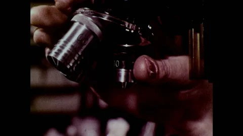 1960s: Man adjusts lenses on microscope. Microscopic organisms. Stock Footage 127731991