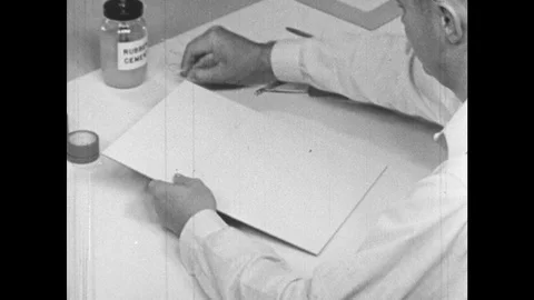 1960s: Man at drafting table runs string through two holes along line on piece Stock Footage 126014969