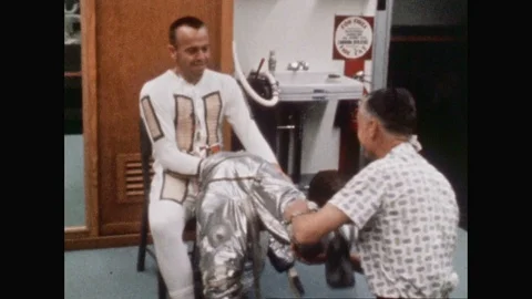 1960s: Man helping Alan Shepard put on suit. Alan Shepard and John Glenn sit Stock Footage 109216616