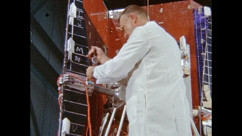 1960s: Man in lab coat adjusts solar panel array arm on satellite. Scientist Stock Footage 95289284