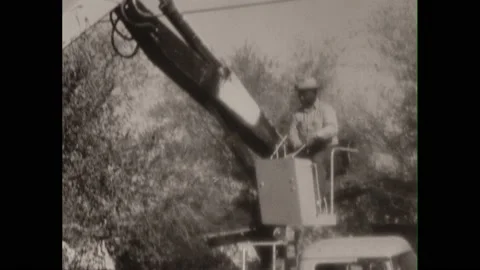 1960s: Man operates small crane, picks up object in bucket, places in dump truck Video stock 213949883