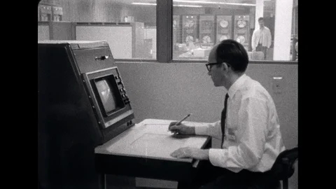 1960s: Man sits in front of computer monitor, drawing on pad on desk, then Stock Footage 110803861