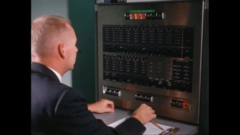 1960s: A man sits before a machine with numerous buttons, lights and switches. Stock Footage 266841759